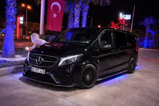 Gece aydınlatılmış bir girişte siyah Mercedes transfer aracı