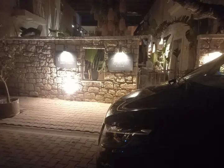 Gece aydınlatılan taş duvarlı girişin yanında siyah transfer aracı