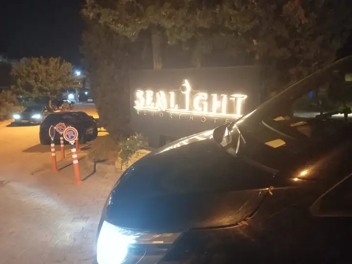 Gece aydınlatılan otel tabelası yanında transfer aracı